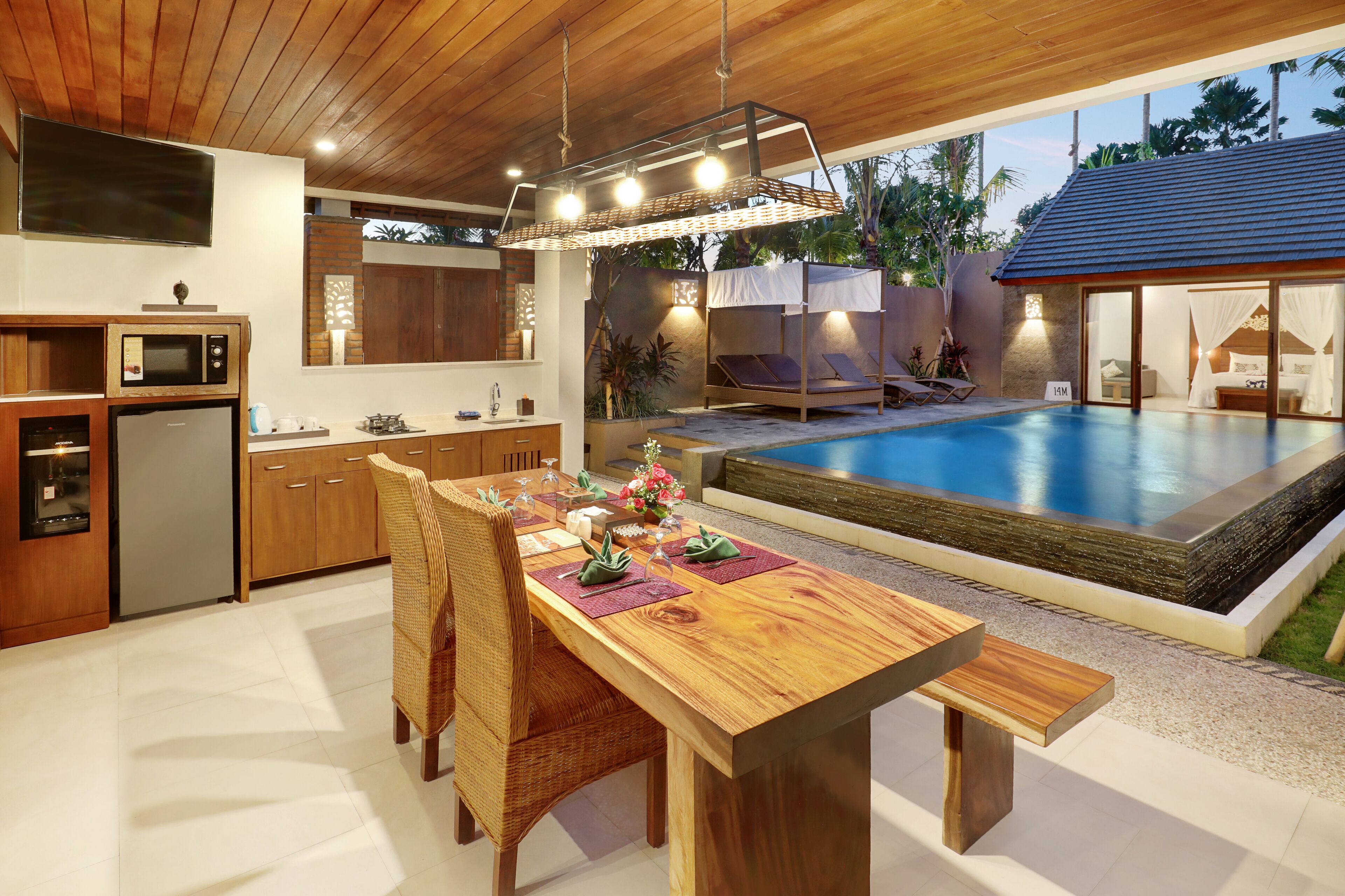 A modern kitchen with built-in appliances, a dining area with a wooden table and chairs, and a poolside seating area with a canopy.