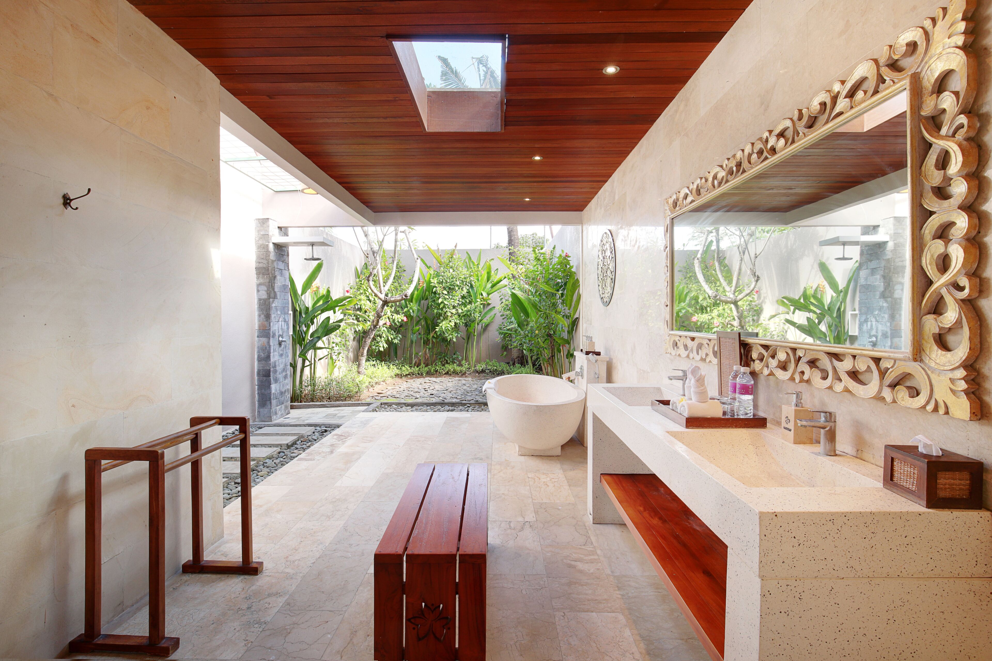A modern bathroom with a large bathtub, a wooden bench, and a large mirror.