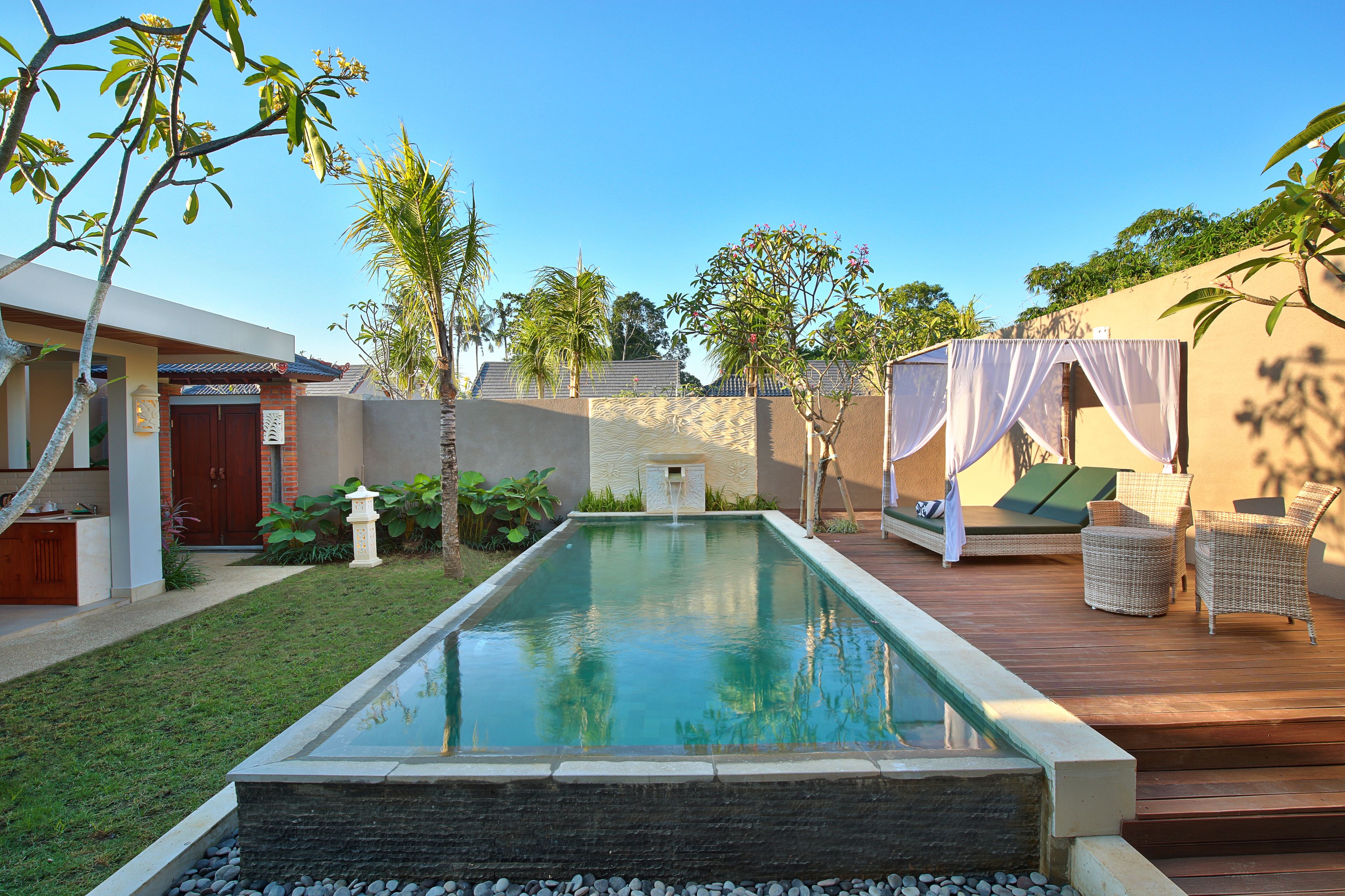 A swimming pool with a wooden deck, lounge chairs, and a covered seating area.