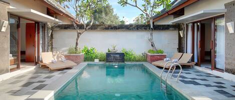 A rectangular pool with a tiled deck, surrounded by lounge chairs and a low brick wall.