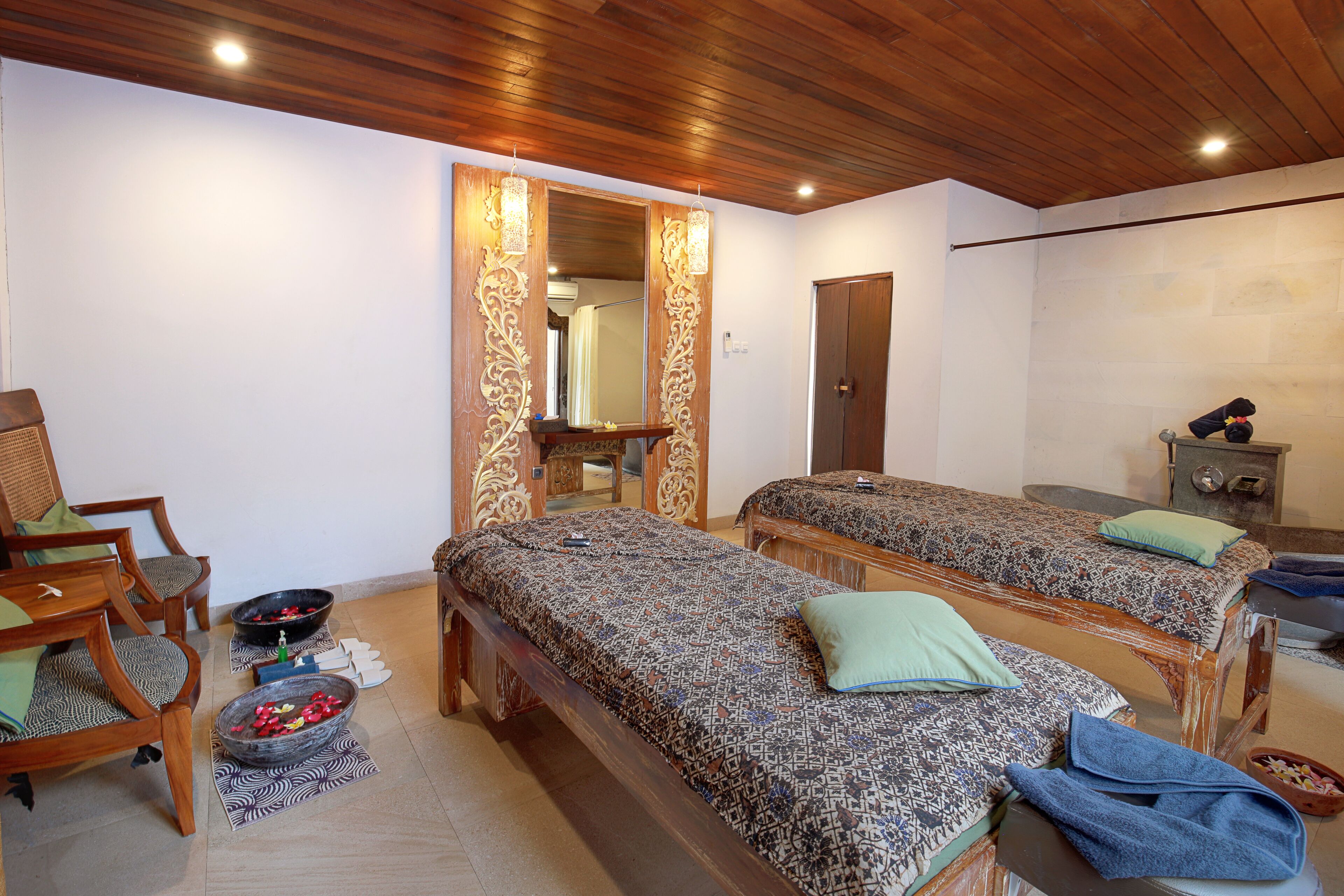 A room with two beds, a wooden ceiling, a mirror, and a small table with a bowl.