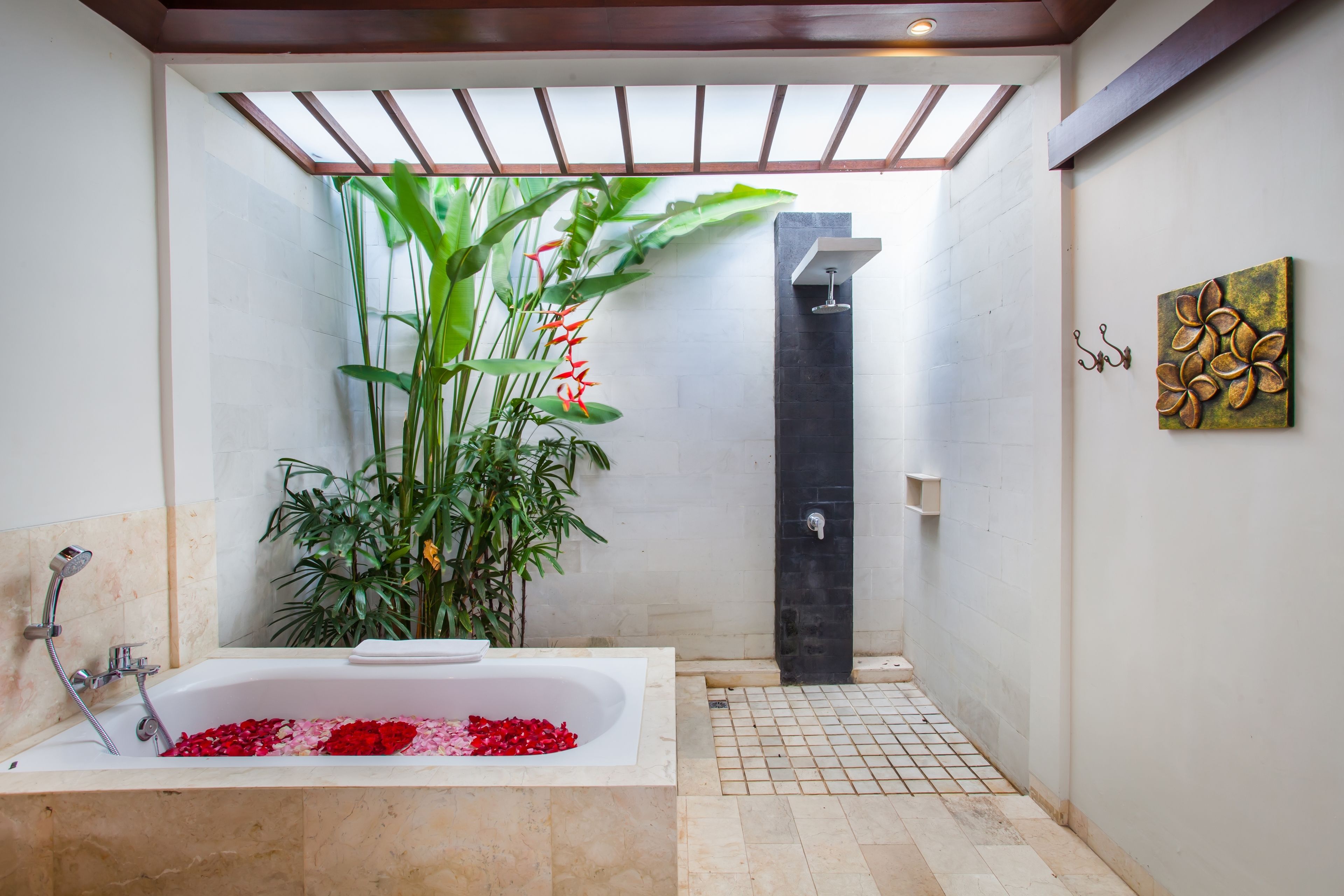 A modern bathroom with a bathtub filled with rose petals, a shower area, and a large potted plant.