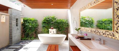 A modern bathroom with a freestanding bathtub, a large mirror, and multiple plants.