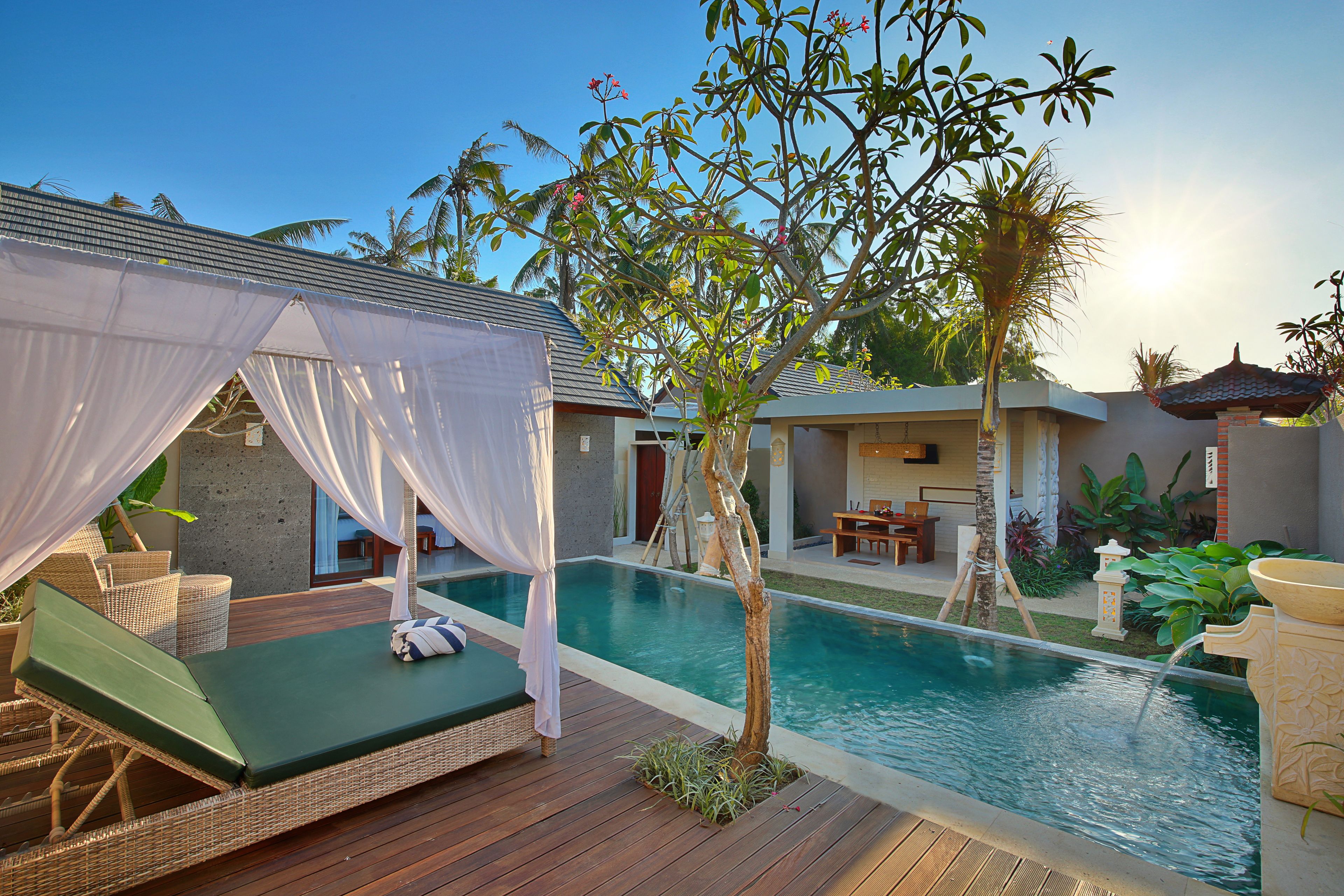 A poolside area with a wooden deck, a canopy bed, and a small tree.