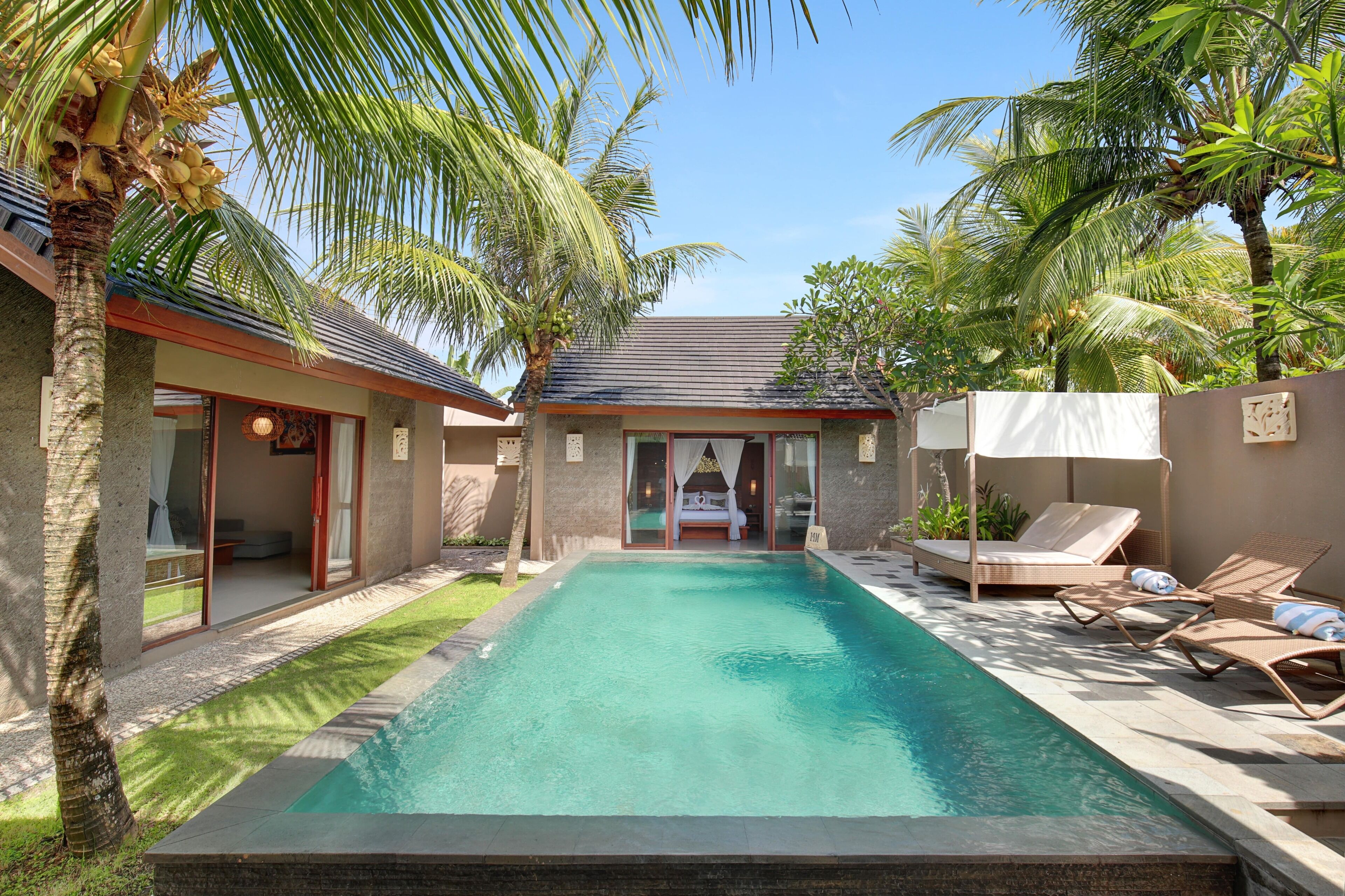 A poolside area with a clear view of the pool, lounge chairs, and a building with a covered seating area.