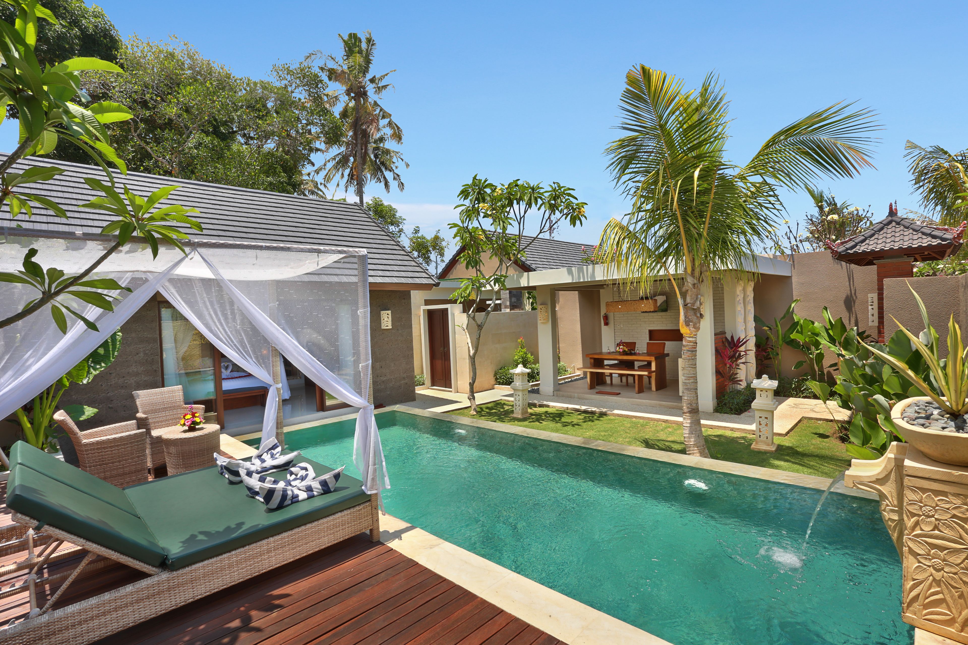 A poolside area with a lounge chair and a small table, surrounded by palm trees and a well-maintained lawn.