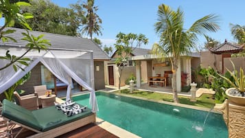 A poolside area with a lounge chair and a small table, surrounded by palm trees and a well-maintained lawn.