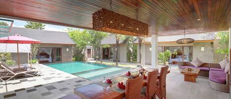A spacious outdoor area with a pool, wooden furniture, and a hanging light fixture.