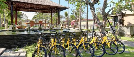 Una fila de bicicletas amarillas estacionadas en un césped, con una fuente y un pabellón al fondo.