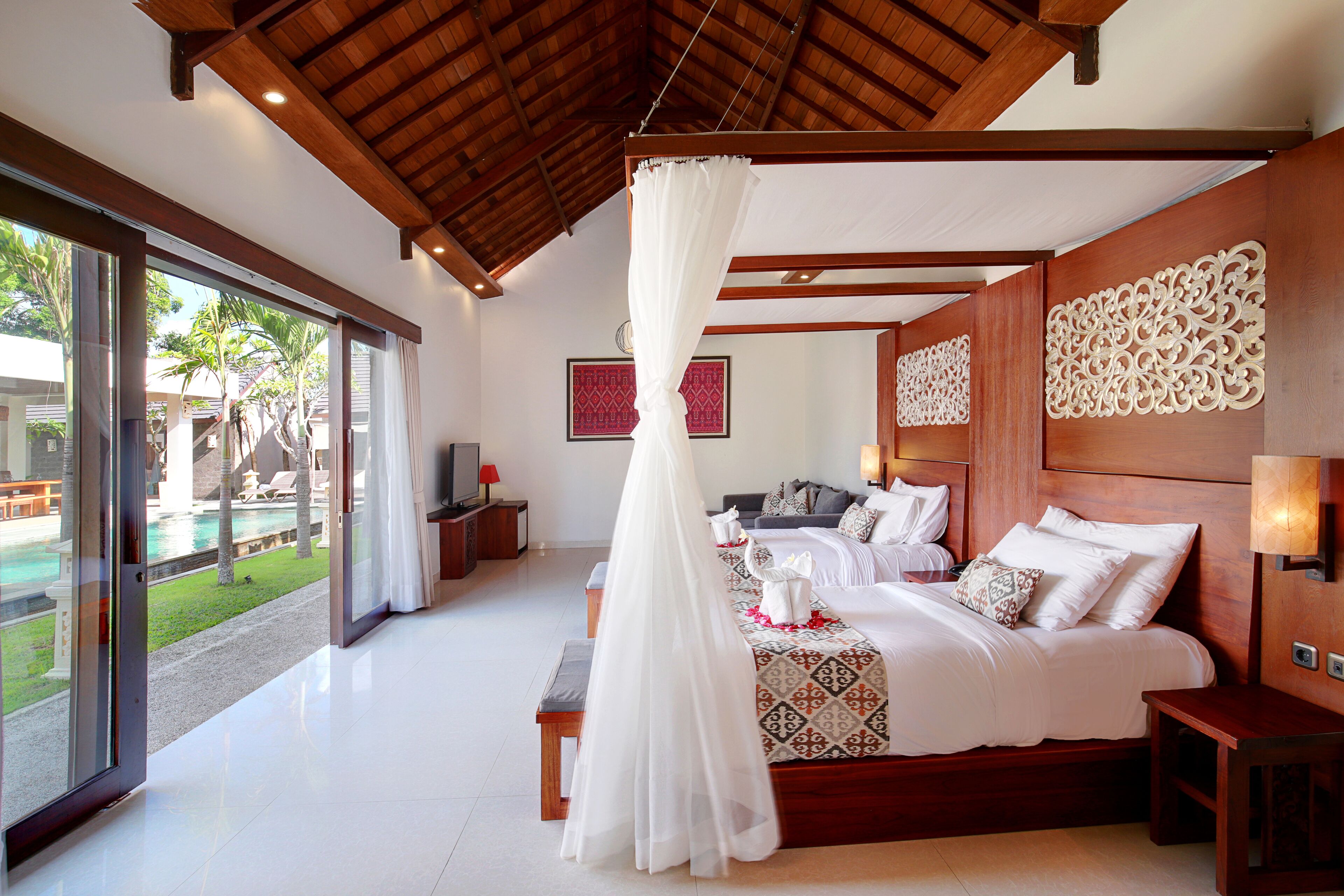 A spacious bedroom with a large bed, a canopy, and a view of a pool and outdoor area.