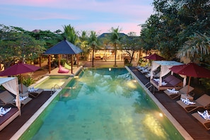 A pool area with lounge chairs and umbrellas, surrounded by lush greenery and a gazebo.
