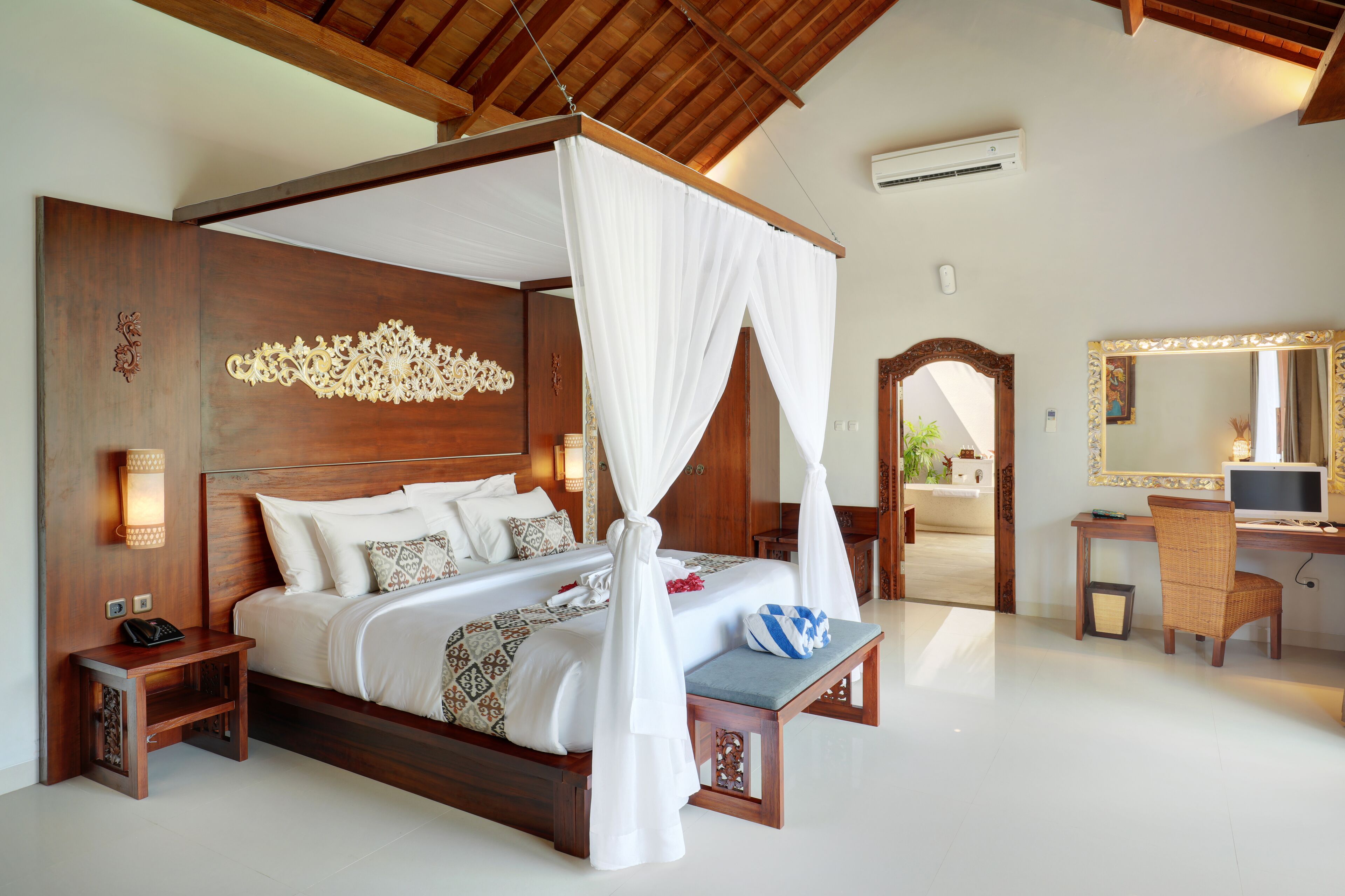 A four-poster bed with white canopy, wooden headboard, bedside tables, and a desk with a chair.