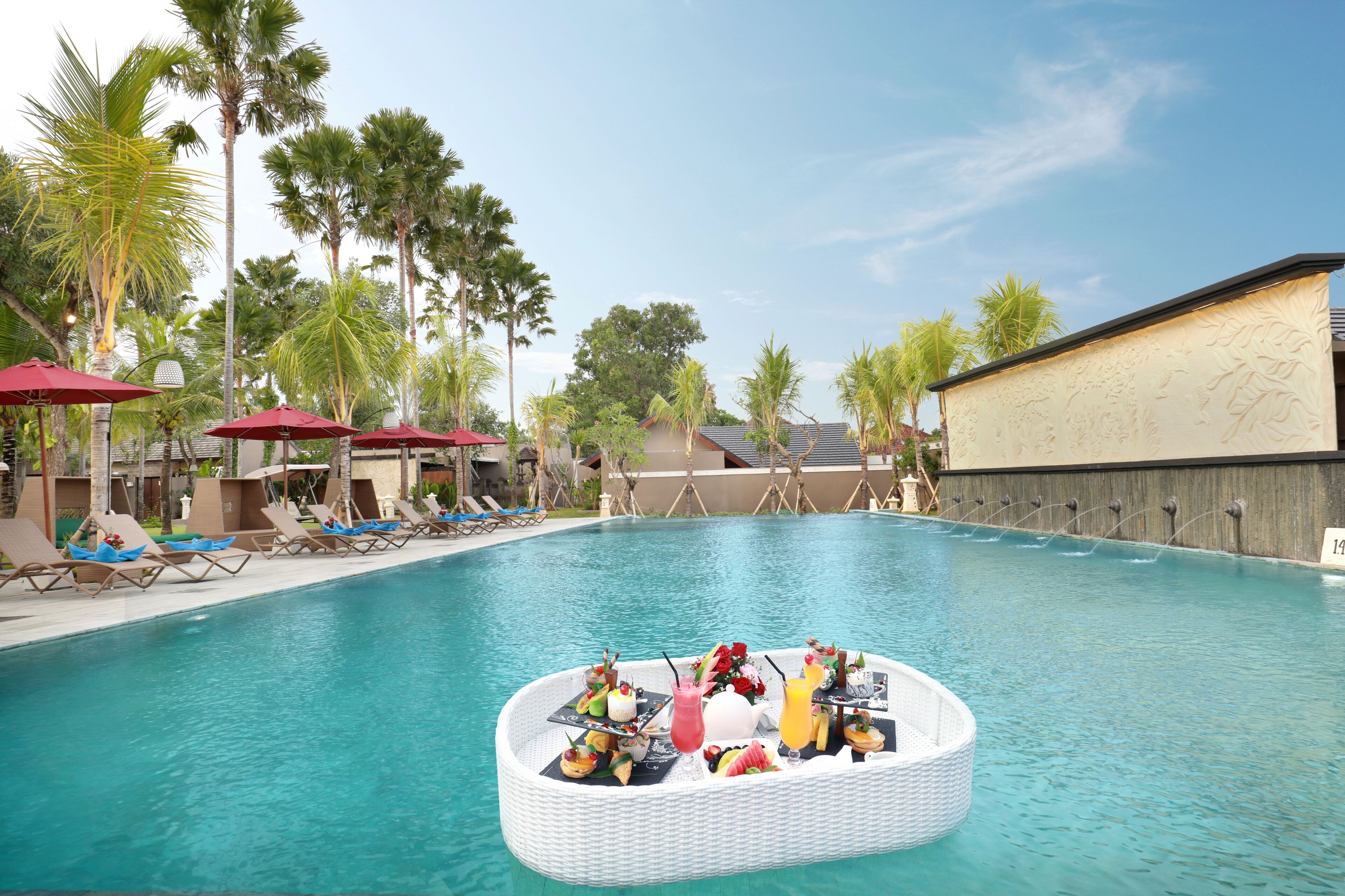 A poolside area with lounge chairs, umbrellas, and a floating bar with drinks.