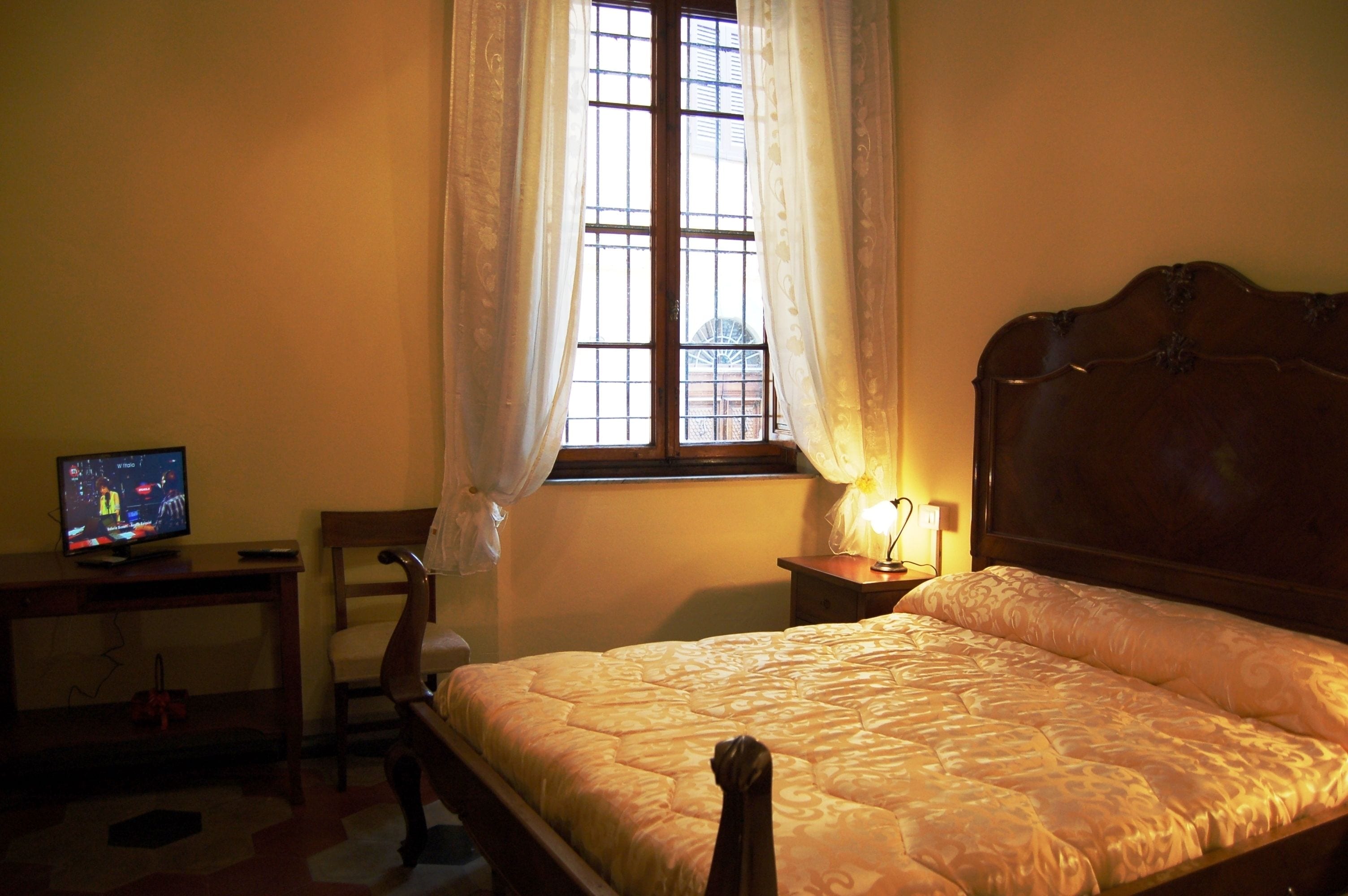 Un dormitorio con cama, escritorio con televisor, silla y ventana con cortinas.