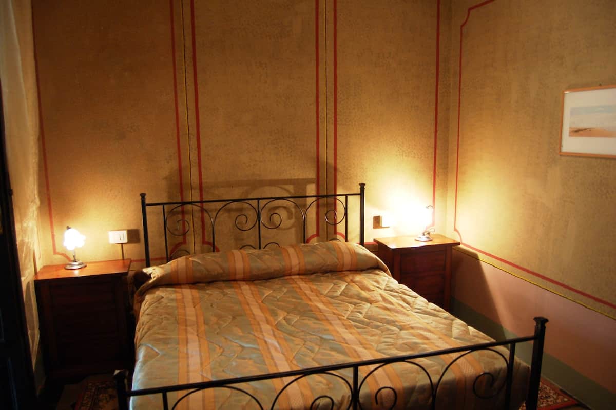 Ein Schlafzimmer mit einem Metallbettgestell, zwei Nachttischlampen und einer gemusterten Bettdecke.