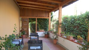 A covered patio with a wooden ceiling, a bench, and potted plants.