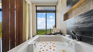 Una bañera de hidromasaje con pétalos de rosa, una ventana con vistas y un perchero para toallas.
