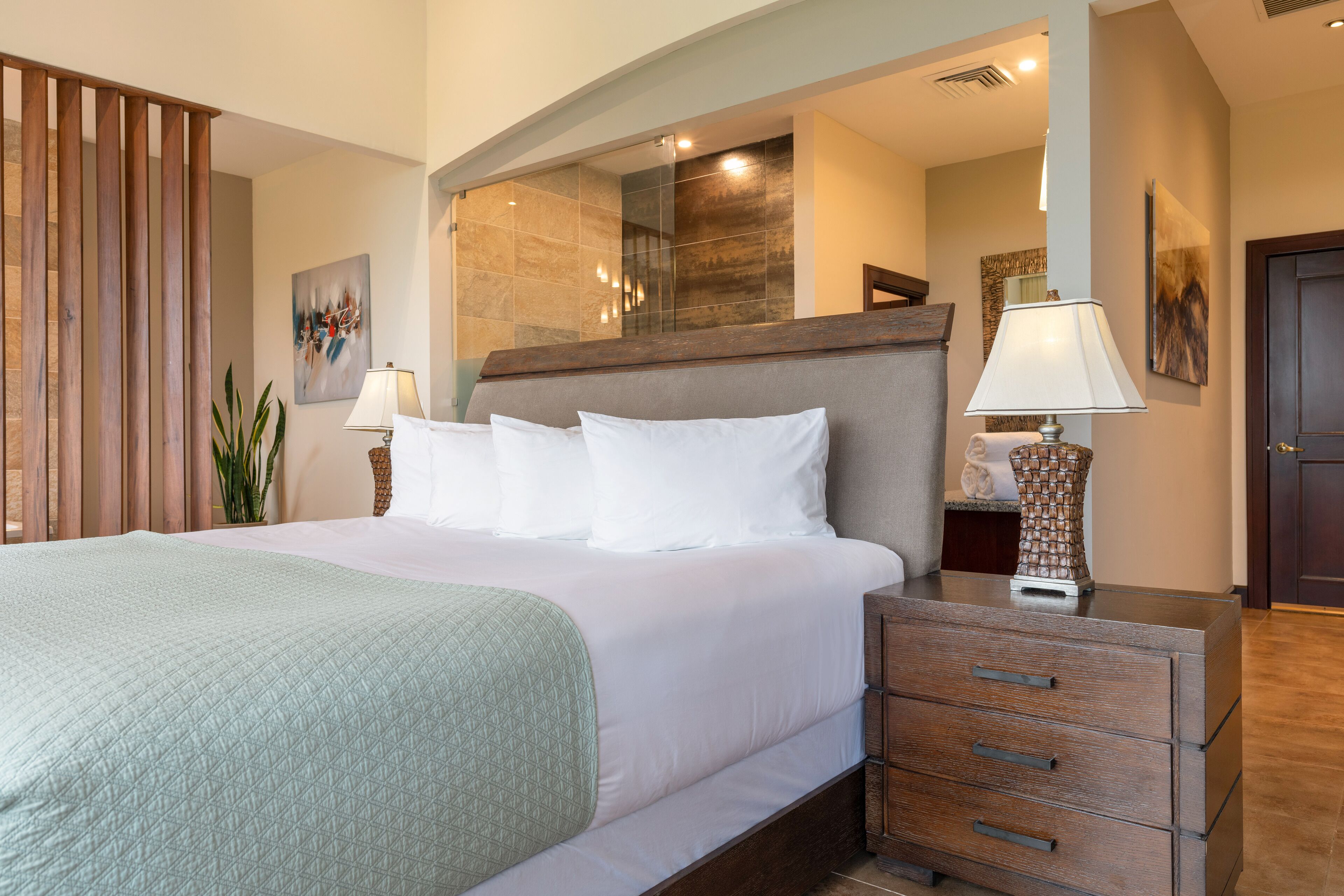 Une chambre d’hôtel avec un grand lit, une tête de lit en bois, une table de chevet avec une lampe et une commode avec des tiroirs.