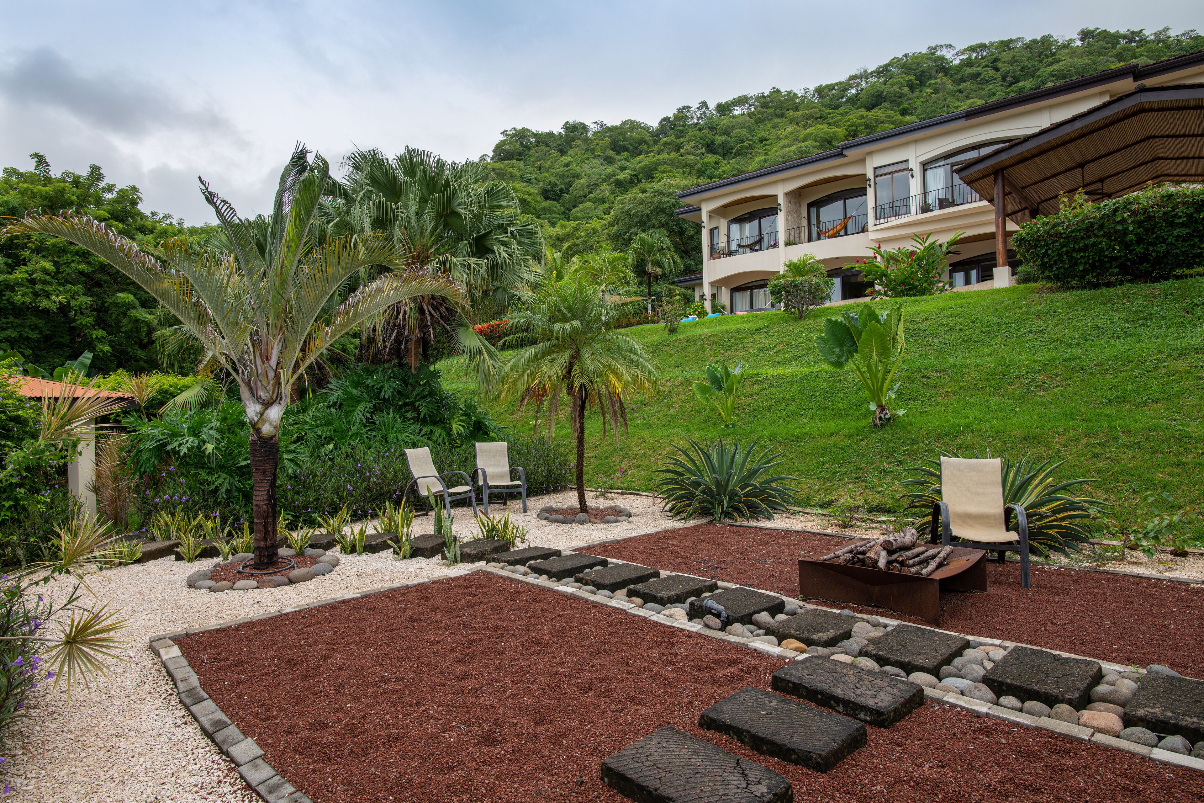 A landscaped garden with palm trees, a fire pit, and outdoor seating.