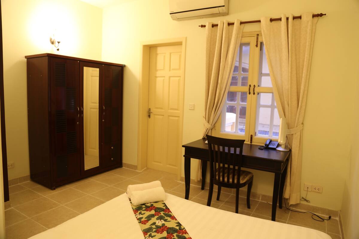 A bedroom with a bed, a desk, a chair, a wardrobe, and a window with curtains.