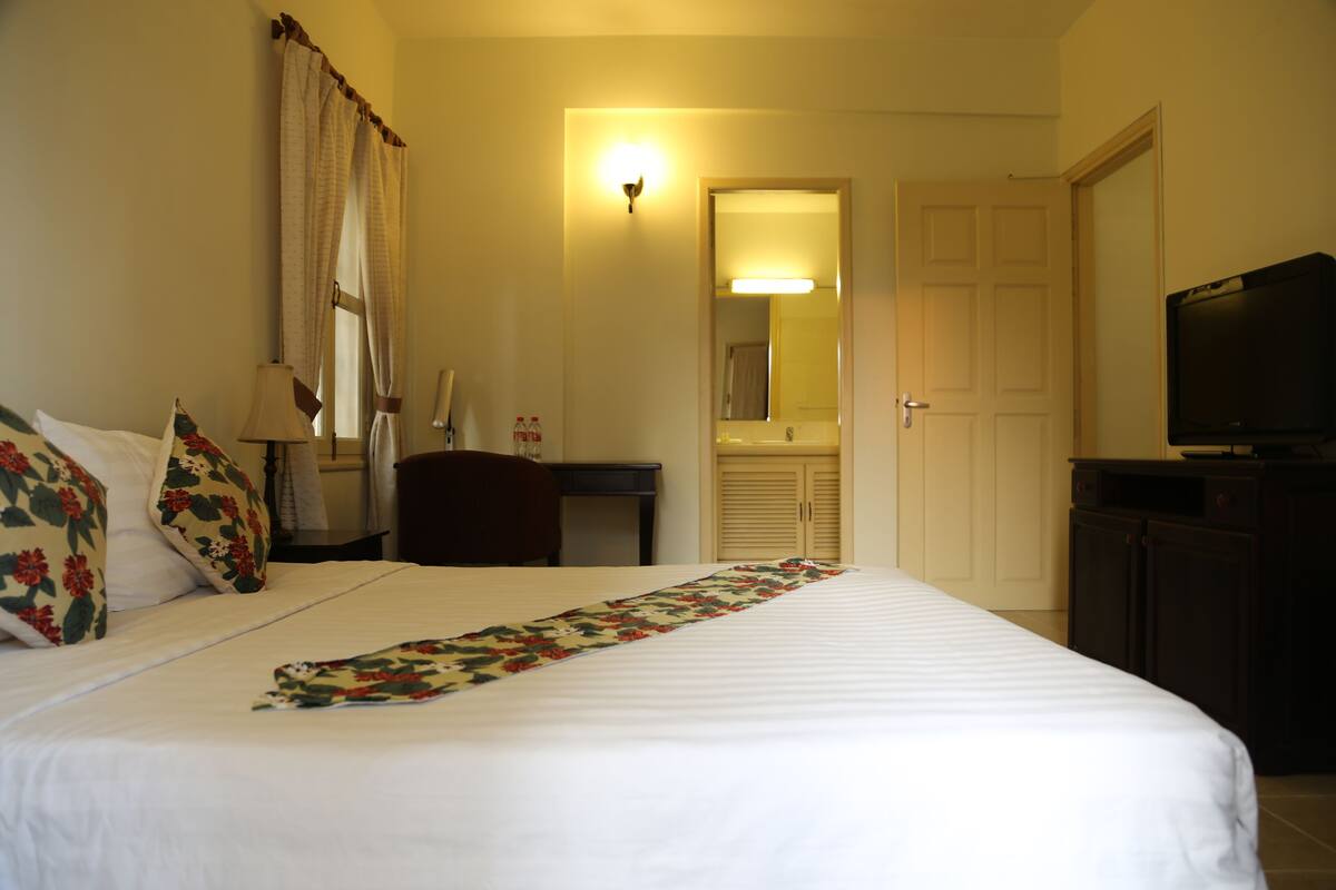 A hotel room with a bed, a desk, a chair, a television, and a bathroom visible through an open door.