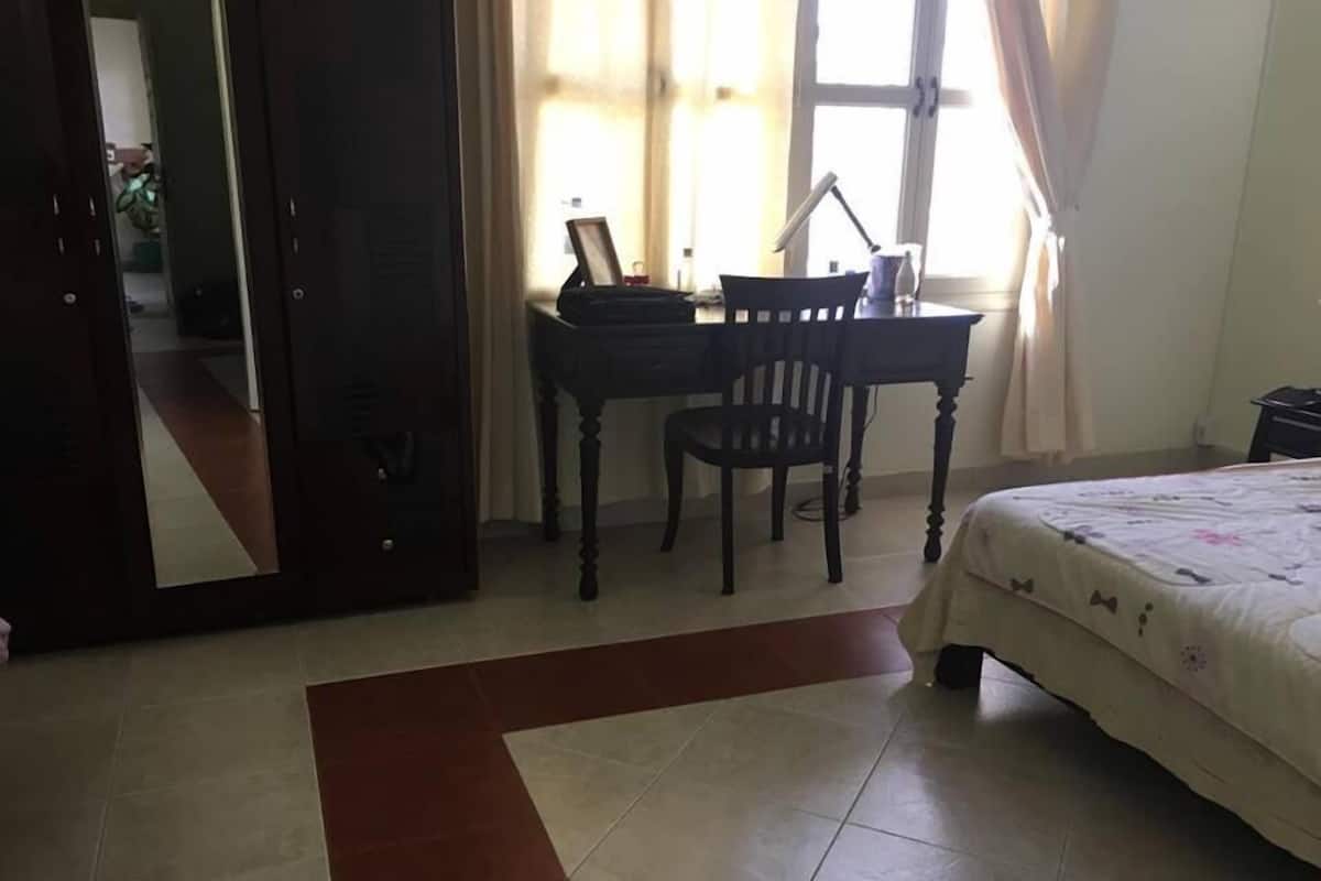 A bedroom with a bed, a desk, and a chair. There is a mirror on the wall, and a window with curtains.