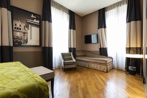 Una camera d'albergo con un letto, una poltrona, un divano, una televisione a schermo piatto e un quadro appeso al muro.