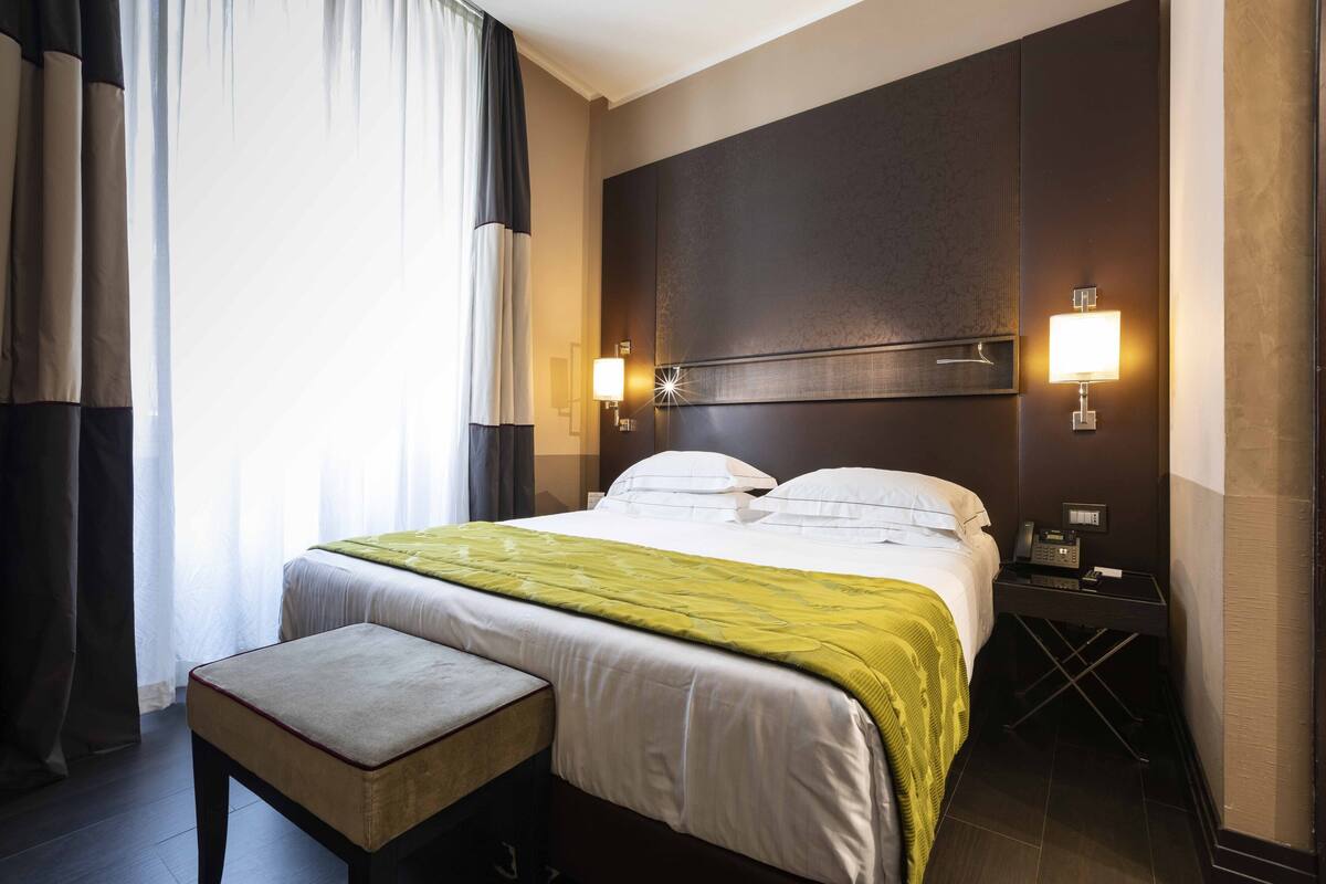 A hotel room with a large bed, bedside tables, a desk, and a window with curtains.