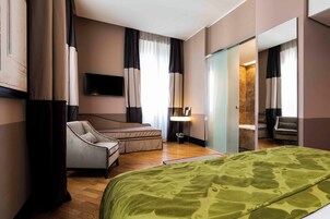 A hotel room with a bed, a chair, a desk, a television, and a mirror.