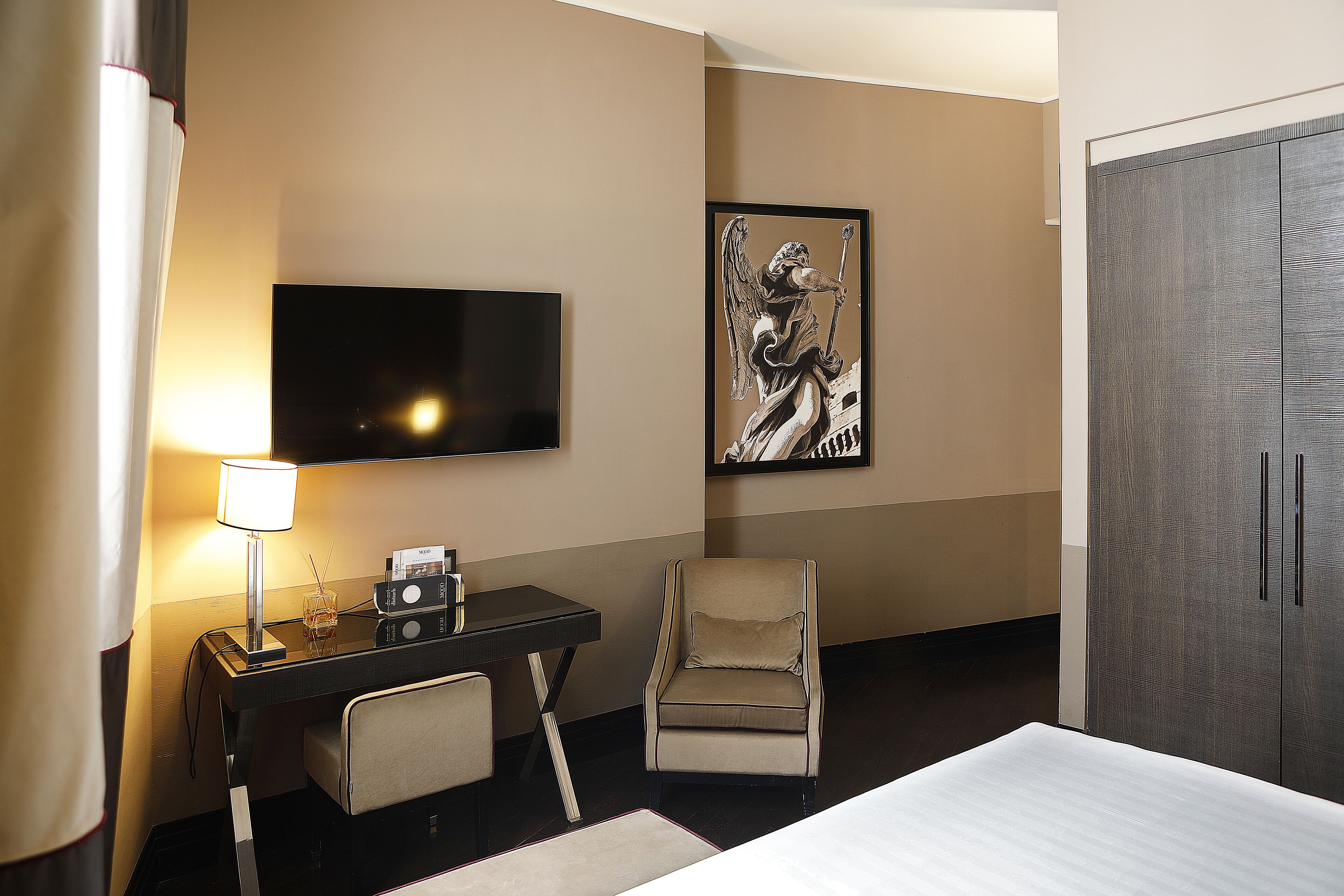 A hotel room with a bed, a desk with a lamp, a chair, a TV, and a wardrobe.
