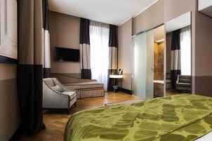 A hotel room with a bed, a chair, a desk, a television, and a mirror.