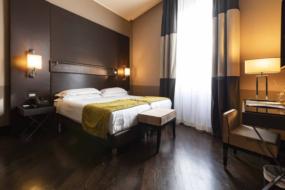A hotel room with a large bed, bedside tables, a desk with a chair, and a lamp.