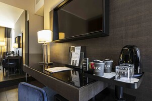 Una moderna camera d'albergo con un'elegante scrivania, un televisore a schermo piatto, una macchina per il caffè e uno specchio.