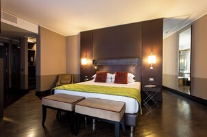 A hotel room with a large bed, two bedside tables, a bench, a chair, a desk, and a mirror.