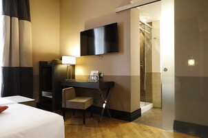 A hotel room with a bed, a desk with a chair, a television, and a shower area.