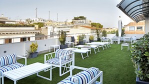 Una terraza en la azotea con mobiliario blanco, césped artificial verde y plantas en macetas.