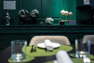Et spiseområde med et grønt bord dækket til to personer, komplet med grøn serviet, hvide tallerkener og et klart glas.
