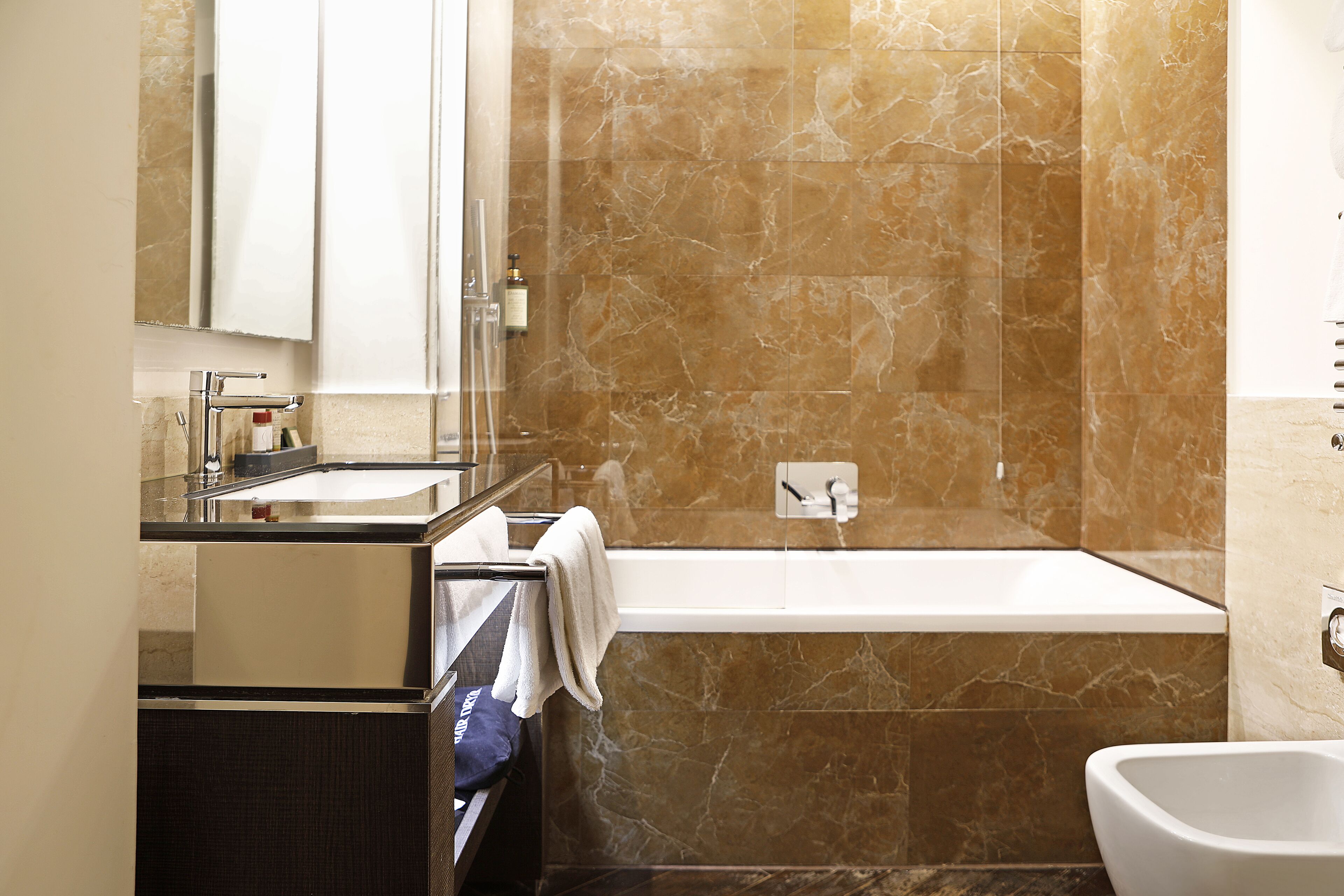A modern bathroom with a marble wall, a bathtub, a sink, and a toilet.