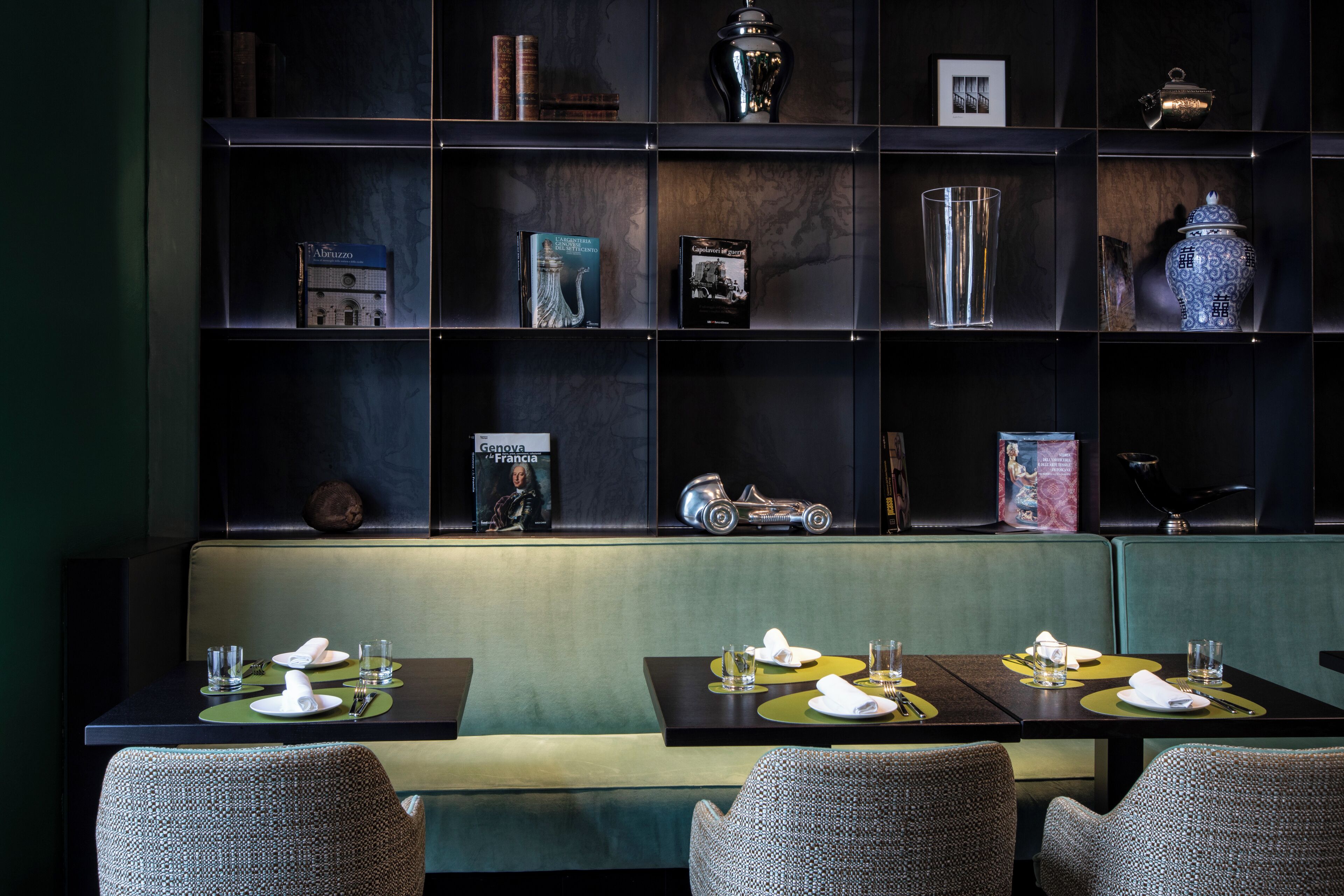 A restaurant with a dark wood bookshelf, green upholstered seating, and neatly arranged tables with white tableware.