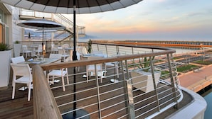 Une terrasse avec des sièges extérieurs, un grand parasol et une vue sur un pont et l’eau.