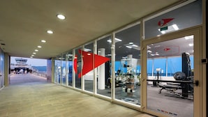 Ein Korridor mit Glaswänden, Blick auf einen Hubschrauberlandeplatz und einem Fitnessbereich.