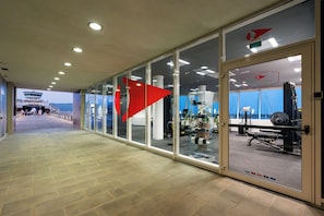 A corridor with glass walls, a view of a helipad, and a gym area.