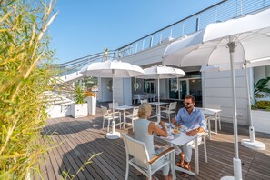 Une terrasse avec des sièges extérieurs, des parasols et une vue sur la rambarde du navire.