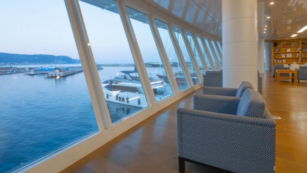 Eine großzügige Lounge mit großen Fenstern und Blick auf einen Yachthafen und Wasser.