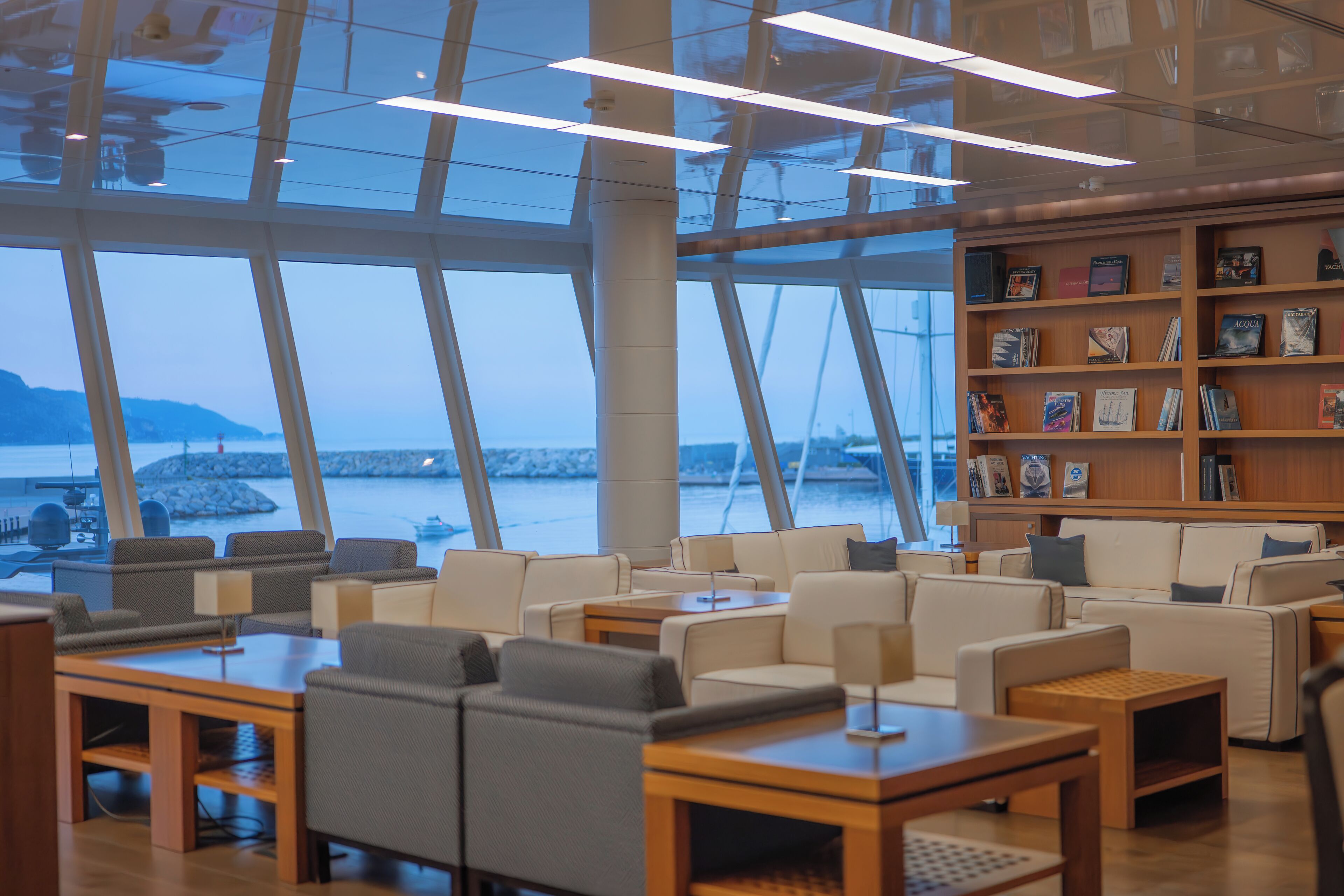 A modern lounge area with seating, tables, and a bookshelf.