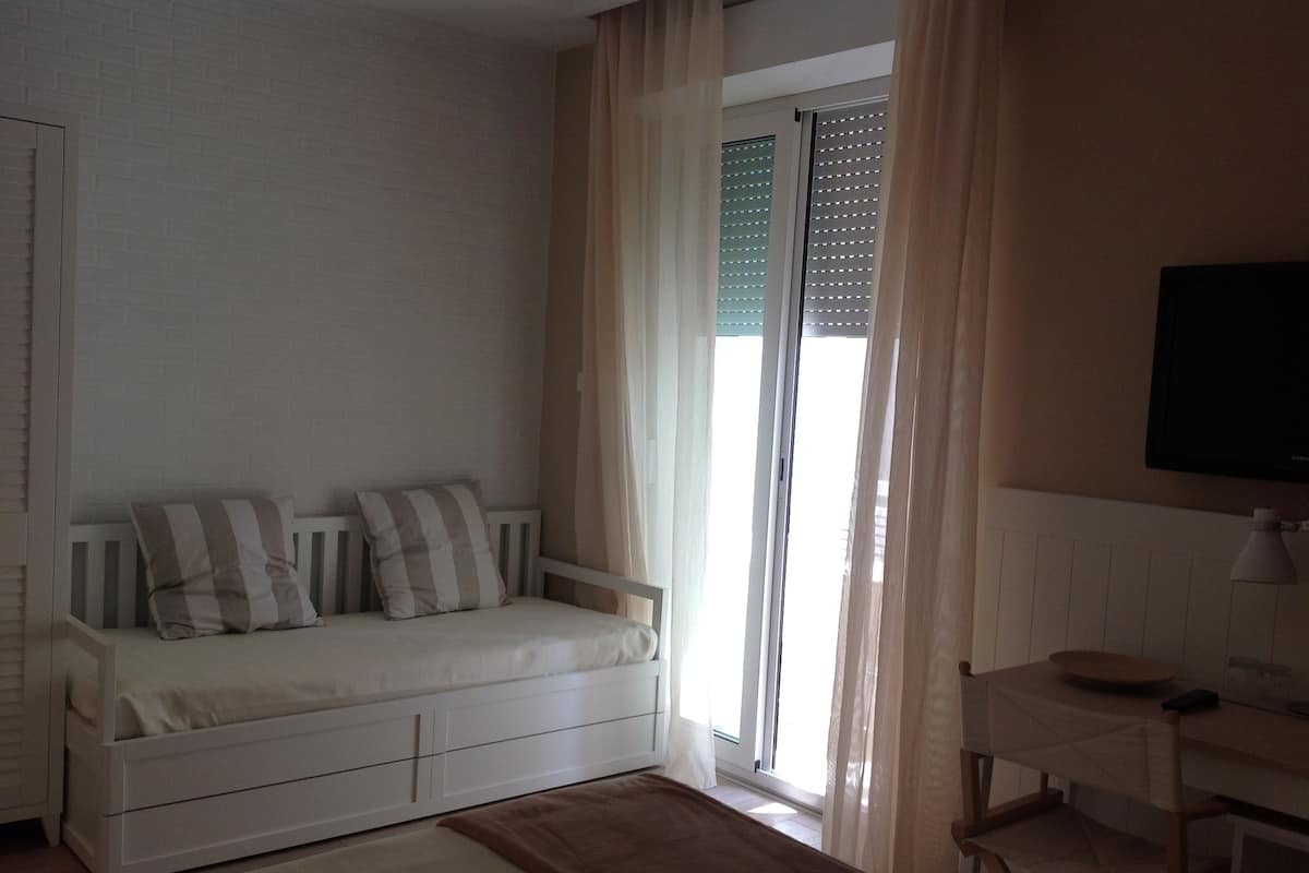 A room with a white sofa, a small desk, and a TV mounted on the wall.