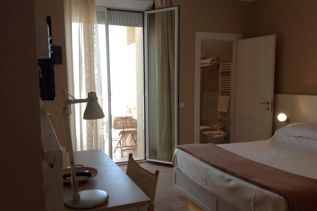 A hotel room with a bed, a desk with a lamp, a chair, and a wardrobe.