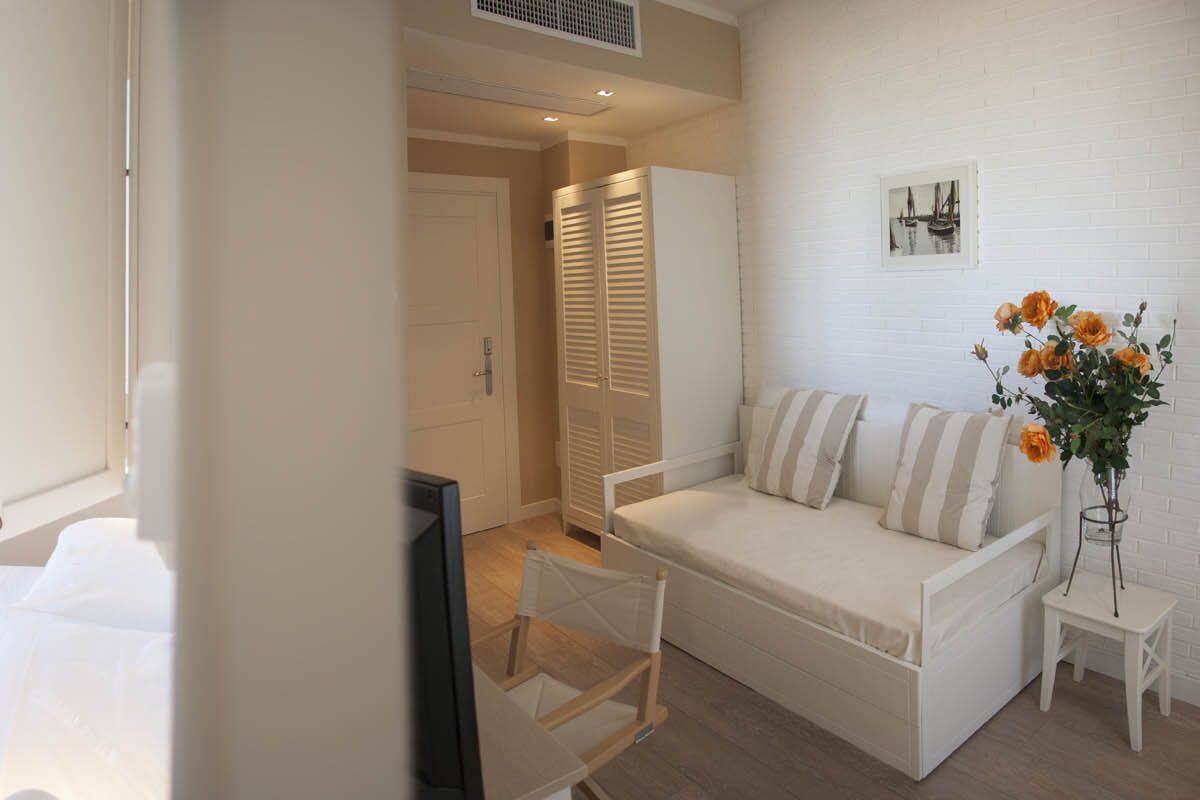 A hotel room with a bed, a sofa, a TV, and a small table with a vase of flowers.