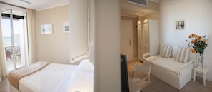 A hotel room with a bed, a sofa, a TV, and a small table with a vase of flowers.
