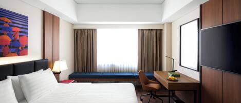 Habitación de hotel con una cama grande, un escritorio con silla, televisor y ventana con cortinas.